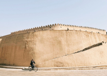 Forteresse historique sur la Route de la Soie en Ouzbékistan avec un cycliste passant devant ses murs imposants.