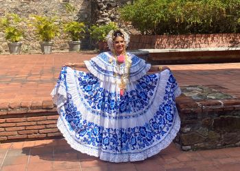 Femme panaméenne souriante en tenue traditionnelle bleue et blanche, posant fièrement dans un cadre naturel pittoresque.