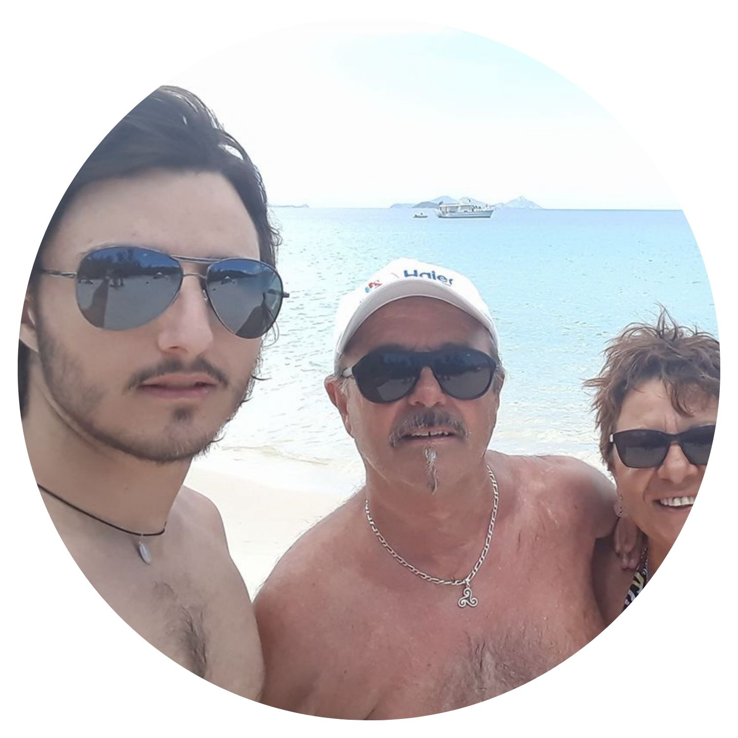 Famille de trois personnes prenant un selfie au bord de la plage en Australie, avec la mer et des cocotiers en arrière-plan.