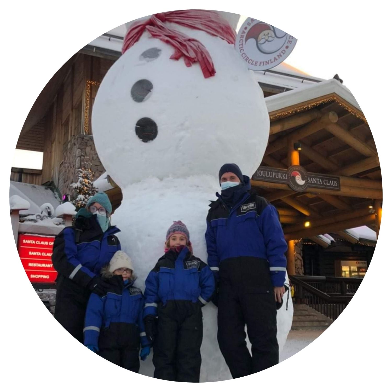 Une famille composée de deux garçons et leurs parents posant pour une photo à côté d'un grand bonhomme de neige en Finlande.