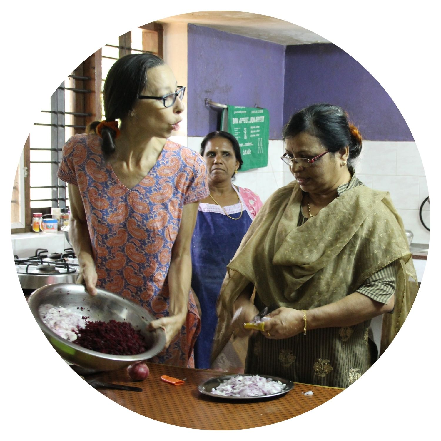 Trois femmes indiennes préparent un repas ensemble dans une cuisine traditionnelle, tout en discutant et partageant des moments de convivialité.