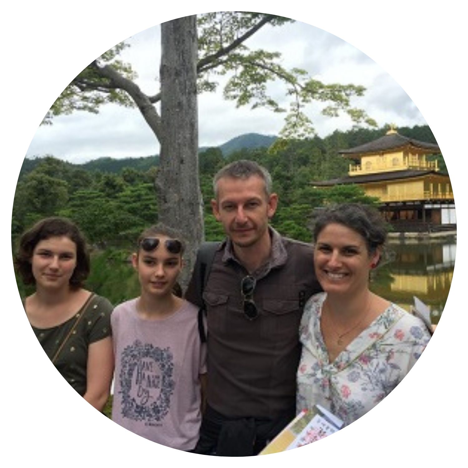 Une famille de quatre personnes, deux filles et leurs parents, posent fièrement devant une maison emblématique au Japon, symbolisant leur voyage familial enrichissant.