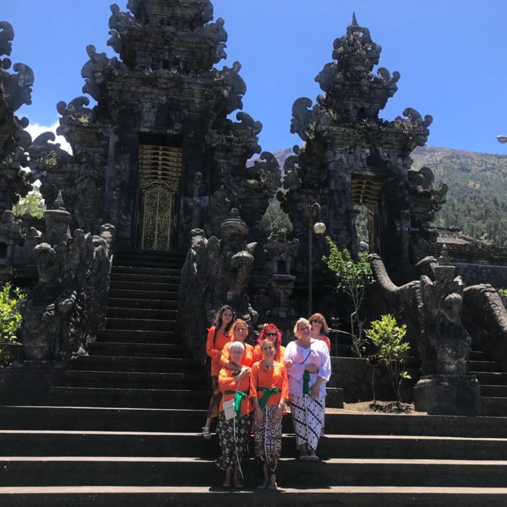 Groupe de femmes vêtues de tenues traditionnelles balinaises, prenant une photo de groupe devant un monument après une visite enrichissante.