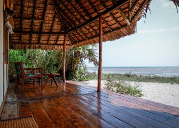 Terrasse couverte d'un bungalow avec vue sur plage de Zanzibar, toit en chaume et mobilier en bois
