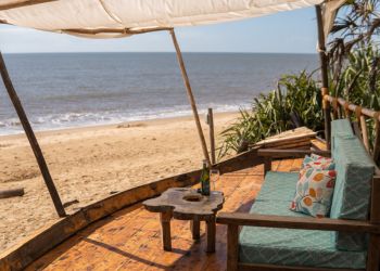Terrasse en bois avec vue sur plage de Zanzibar, parasol en toile, canapé confortable et table basse pour apéritif en famille